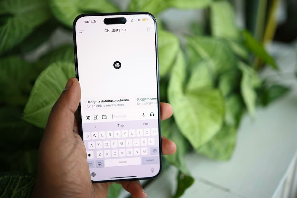 Smartphone displaying the ChatGPT app interface with artificial intelligence prompts on screen and plants in the background.